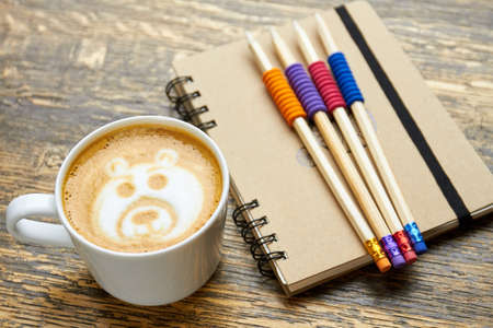 Coffee, pencils and notebook. Latte foam art. Is caffeine good for studying.の写真素材