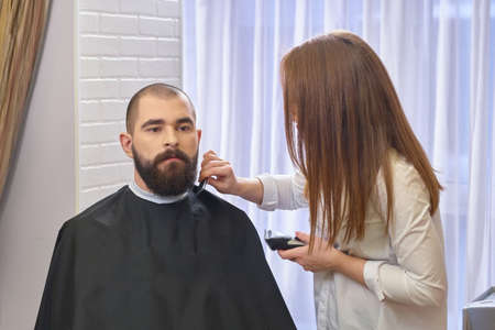 Beard grooming in salon. Female barber working. Barber shop jobs.の写真素材