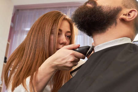 Female barber is grooming beard. Barbershop employee at work.の写真素材