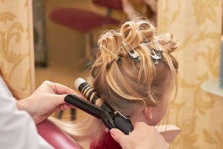 Hairdo of little girl. Hands using curling iron.の写真素材