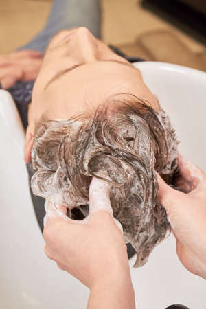 Hands washing hair with shampoo. Hair of barber shop customer. Professional shampoo brands.の写真素材