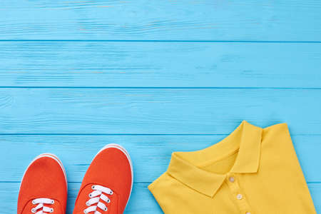 Cropped image of colored clothing. Shoes, t-shirt, blue wooden surface.の写真素材