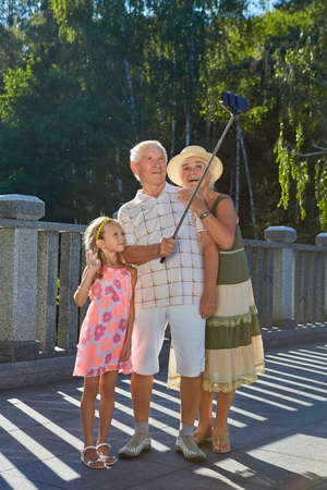 Happy grandparents and grandchild, selfie. People on summer park background. Technologies in daily life.の写真素材