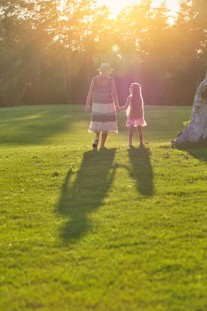 Girl with grandmother, back view. People, green grass and sun.の写真素材