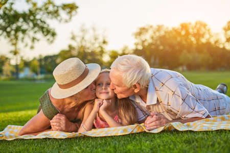 Grandparents kissing granddauther. People lying outdoors. Love to grandchildren.