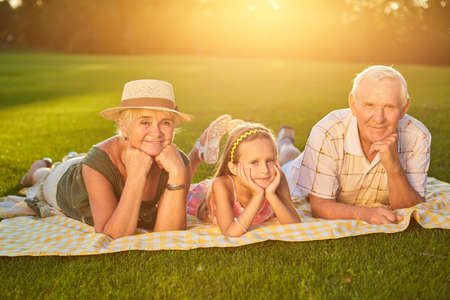 Happy grandparents with grandchild. People lying outdoors summer.