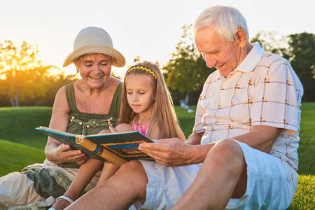 Child with grandparents, photo album. Happy people looking at photos.
