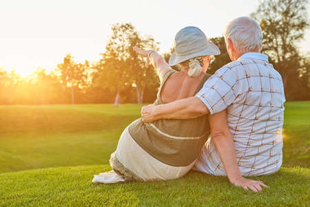 Couple sitting on grass, summer. Old man and woman.の写真素材