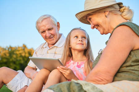 Child with a tablet, grandparents. Happy grandma looking at granddaughter.の写真素材