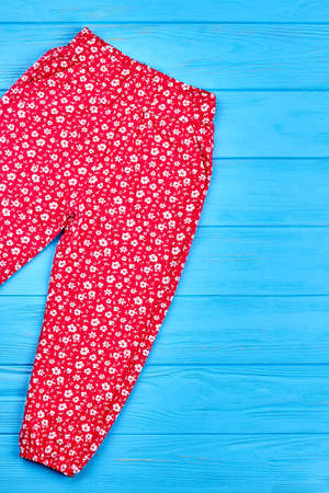 Fashionable summer baby girl pants. Vertical image of kids girl red patterned trousers lying on blue wooden background.の写真素材