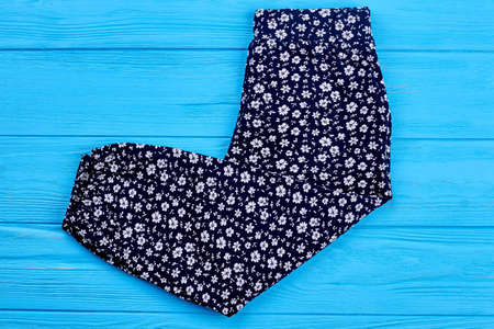 Baby girl pants in vintage print. Folded dark blue baby girl trousers in white flowers on blue wooden background.の写真素材