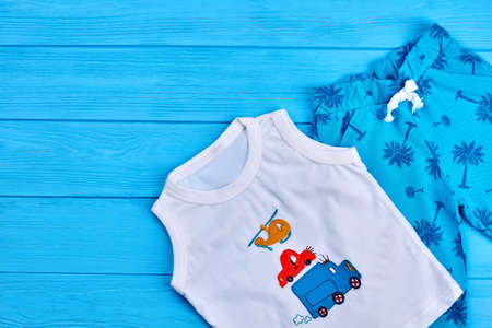 White cotton baby boy t-shirt. Organic toddlers boy summer clothing on blue wooden background. Modern baby boy clothes on sale.の写真素材