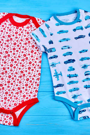 Two cute newborn cotton bodysuits. Dainty design infant boys and girls natural rompers on blue wooden background, top view. Infant baby summer outfit.の写真素材