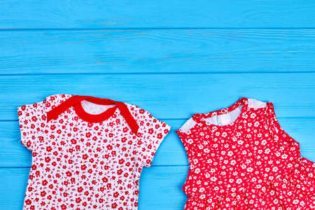 Cute baby girl summer wear. Infant girl printed bodysuit and dress on blue wooden background, copy space. Casual clothing for infant baby girl.の写真素材