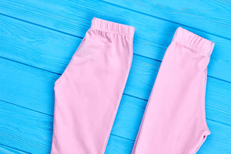 Set of baby-girl pink leggings. New cotton pants for infant girls folded on blue wooden background. Baby-girl brand clothes.の写真素材