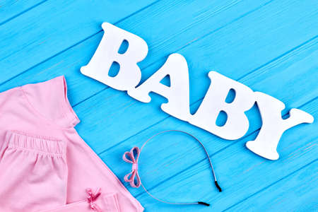 Baby-girl summer fashion background. Infant girl cotton clothes, hair accessory, inscription baby, blue wooden background.の写真素材