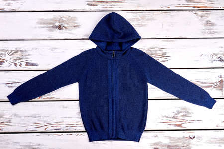 Dark blue hooded knitted pullover. Children new zipper sweater on old wooden background. Boys knitted outfit.の写真素材