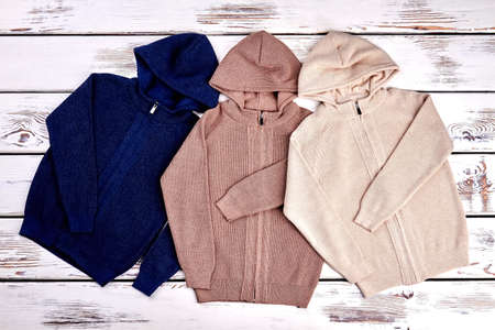 Collection of new knitted hooded sweaters. Set of cute hooded knit cardigans on old wooden background. High quality cotton pullovers.の写真素材