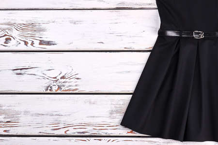 Cropped image of vintage black dress. Classical short a-line dress with belt for little girls on white wooden background, copy space. Little black retro dress.の写真素材