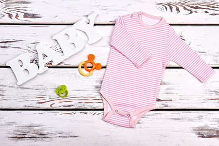 Baby-girl pink stripes bodysuit. Newborn baby-girl cotton soft striped bodysuit, accessories on old wooden background, top view.の写真素材