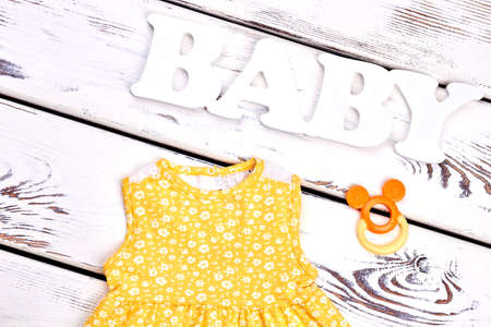 Baby-girl boutique clothes, accessories. Infant girl new cotton sundress, teether, old wooden background, top view. Kids clothing on sale.の写真素材