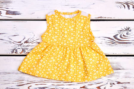 Baby-girl cute yellow cotton dress. Toddler girl sleeveless patterned top on white wooden background.の写真素材