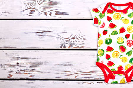 Baby modern design cotton bodysuit. Newborn kids soft fruit print bodysuit on wooden background, copy space. Baby fashion outfit.の写真素材