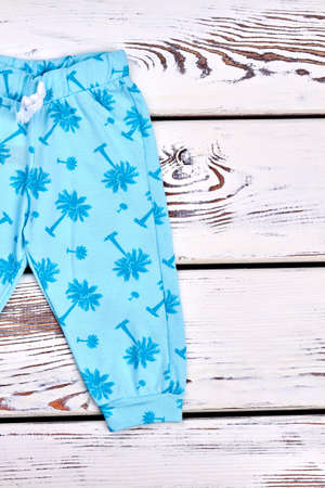 Baby-girl blue patterned harems. Toddler girl blue pants with a pattern of palm tree, wooden background, top view. Kids summer fashion style.の写真素材