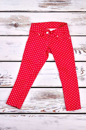 Girl red patterned cotton trousers. Childrens new colored trousers with a pattern of small white hearts, white wooden background. Kids fashion style.の写真素材