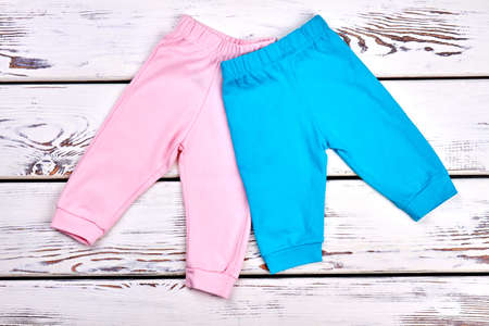 Collection of new kids trousers. Infant girls and boys colored pants on white wooden background. Childs organic apparel on sale.の写真素材