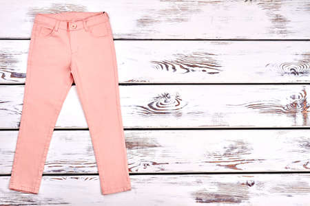 Teen girls modern summer trousers. Female slim peach color pants on white wooden background, copy space. Woman summer fashion outfit.の写真素材