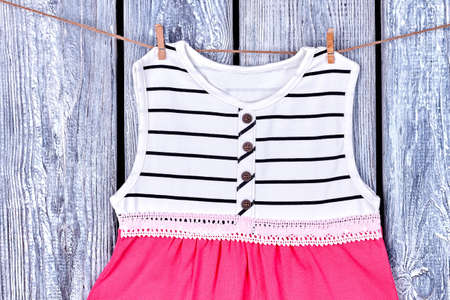 Baby dress hanging on clothesline. Infant girl elegant dress drying on rope, grey wooden background.の写真素材