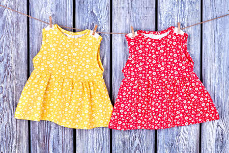 Kids dresses hanging on rope. Baby-girl apparel drying on clothesline, old wooden background.の写真素材