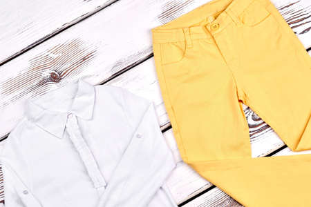 Girls high quality cotton garment. Teen girl beautiful long sleeve blouse, yellow skinny pants on wooden background. Childrens clothes on sale.の写真素材