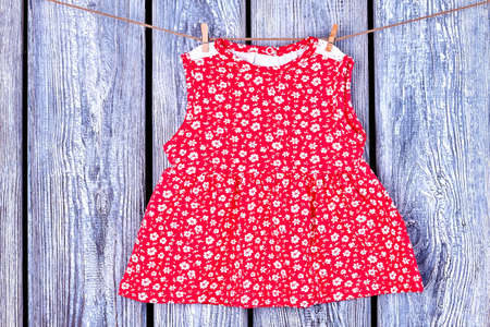 Baby red dress hanging on clothesline. Toddler girl patterned top drying on rope on vintage wooden background. Wet kids apparel in laundry.の写真素材