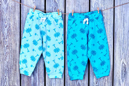 Kids trousers hanging in laundry. Childs summer pants drying on rope on old wooden background. Purity of infants garment.の写真素材