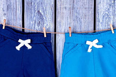 Kids pants hanging on rope. Childrens cotton shorts drying on clothesline on old wooden background.の写真素材