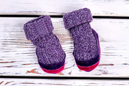 Kids knitted woolen room slippers. Childs warm purple winter socks on white wooden background. Childrens narural handmade garment.の写真素材