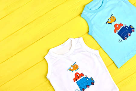 Infant boys summer colored apparel. Set of trendy cartoon t-shirts for toddler boys on yellow wooden background, top view. Kids summer apparel on sale.の写真素材