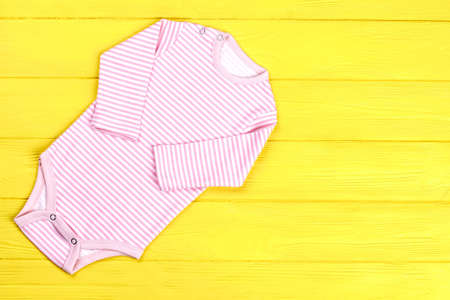 Baby-girl striped cotton romper. Infant girl high quality bodysuit on yellow wooden background, top view, copy space.の写真素材