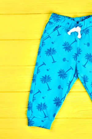 Kids beautiful blue harems. Infants brand cotton trousers on yellow wooden background. Toddlers brand apparel on sale.の写真素材