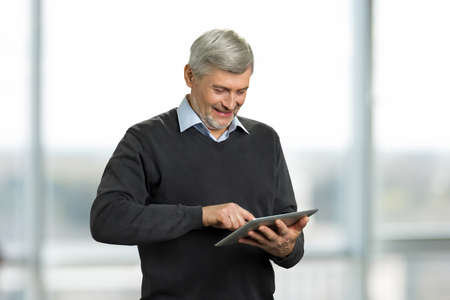 Mature man working on computer tablet. Smiling senior man with digital tablet on blurred background.の写真素材