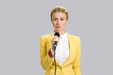 Young woman in formal wear with microphone. Young business woman public speaking isolated on grey background.の写真素材