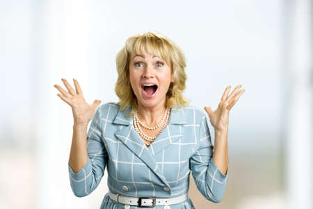 Surprise mature woman with good news. Close up portrait of white-skin woman looking shocked and excited in full disbelief with open mouth and raised hands.の写真素材