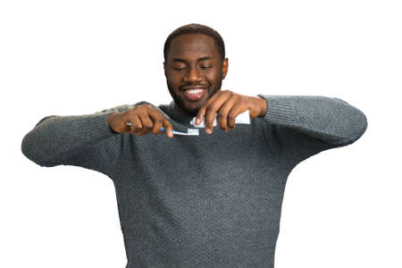 Black man applying toothpaste on a toothbrush. Attractive man looking down on toothpaste and brush on white background. Taking care of teeth and mouth.の写真素材