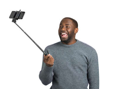 Happy young man taking selfie. Cheerful afro american guy taking picture with monopod on white background.の写真素材
