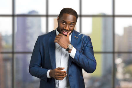 Afro american businessman touching chin. Smiling young black man with hand near his chin. Black boss of corporate company on blurred background.の写真素材