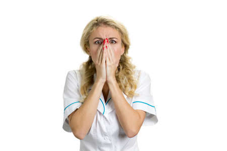 Desperate and shocked young nurse. Surprised woman in white uniform looking scared and horrified covering her face with hands on white background. Human facial expressions.の写真素材