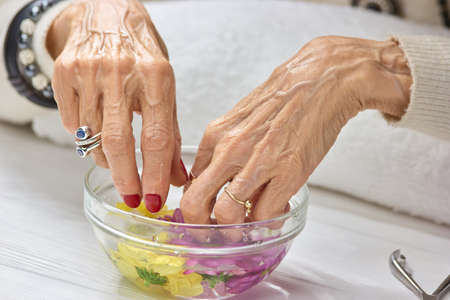 Spa treatment for female hands. Old woman hands having manicure and spa. Caucasian woman hands in bowl with water. Nail care concept.の写真素材