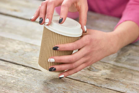 Female hands opening cardboard coffee cup. Young woman hands opening disposable cup with coffee. Time to drink coffee.の写真素材